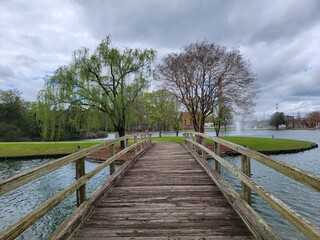 Rustic Wooden Footbridge Over Pond with Fountain and Trees on Overcast Day