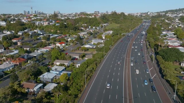Aerial view of traffic on a highway in Auckland, New Zealand. Cars are commuting on a sunny day, with residential areas and the city skyline in the background.