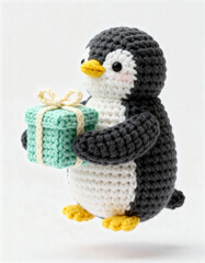 Handmade crochet penguin holding a green gift box with a cream ribbon, isolated on a white background