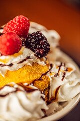 A close up of fried ice cream topped with whipped cream, chocolate, blackberries and raspberries at a modern food restaurant 