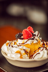 A close up of fried ice cream topped with whipped cream, chocolate, blackberries and raspberries at a modern food restaurant 