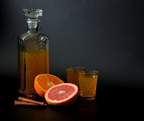 Grapefruit-orange liqueur with cinnamon and anise, homemade alcohol in a crystal bowl on a black background, next to ripe fruits and spices.