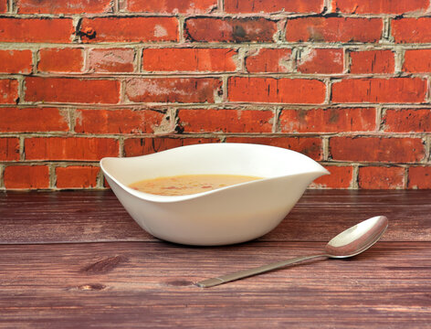 Delicious and nutritious cheese cream soup with smoked meat in a deep ceramic plate on a wooden table, a tablespoon nearby.