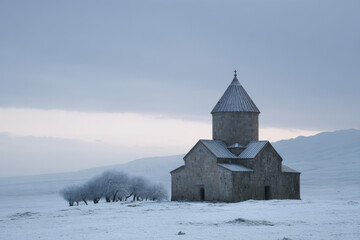 Fototapeta premium stone church stands majestically in snowcovered field under grey overcast sky