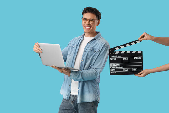 Male screenwriter holding laptop and female hands with movie clapper on blue background