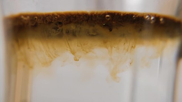 Instant coffee granules falling into hot water and dissolving with spoon stirring, macro shot. Morning routine concept