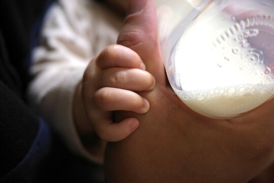 Optimal English Title: Modern Asian father feeding baby with milk bottle, promoting parental leave and family bonding