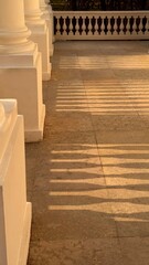 Golden hour light casting dramatic, sharp shadows from a white balustrade onto the tiled palace terrace floor in a classic architectural setting