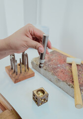 Female craftswoman using a metal punch on a polishing block to shape a jewelry component in a craft workshop.