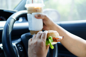 Asian woman driver hold and eat hamburger food in car.