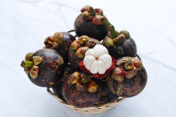 A basket filled with fresh mangosteens, with one opened to show the white fruit inside.