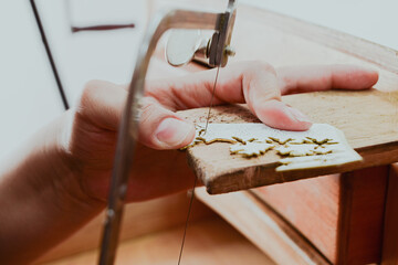 Jeweler artisan hands cutting metal with jeweler saw on wooden workbench in craft workshop,...