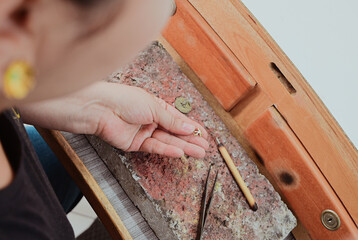 Jeweler artisan hand holding small metal jewelry piece on workbench with tools and firebrick,...