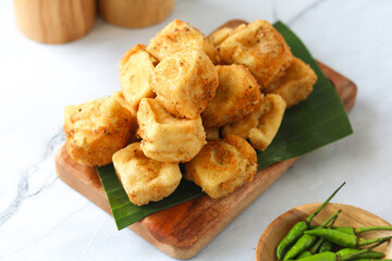 Crispy golden-brown fried tofu, a beloved and classic Indonesian snack arranged on a traditional wooden tray and banana leaf with green chili (cabe rawit). Captured with natural light.