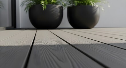 Close up of a modern composite deck with two dark planters holding lush green plants in soft natural light