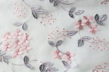 A white sheer fabric embellished with pink and gray lace embroidery. The floral and leafy patterns...