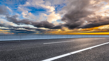 Fototapeta premium Empty asphalt road and dramatic sky clouds at sunset