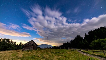 Dramatic Night Sky with Moving Clouds Over a Rustic Barn in a Mountain Landscape.