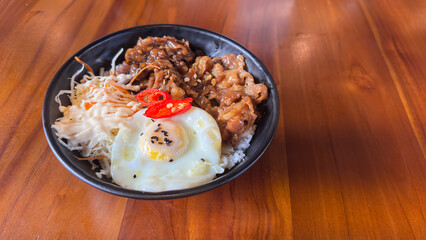 Bowl of Asian-style Rice Dish with Fried Egg, Sliced Beef, and Vegetables on Wooden Table