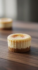 Small baked cheesecake dessert rests on a dark wooden surface with another blurred dessert in the background