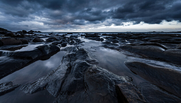 Dark rocky shore with tide pools under stormy skies.