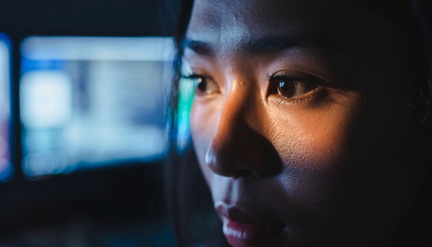 Woman's face illuminated by screen light in dark room - Powered by Adobe