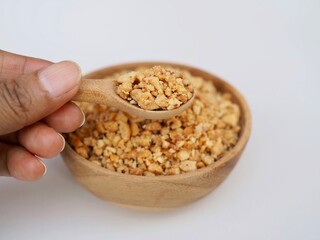 Crushend peanuts in a wooden spoon and a wooden cup placed on a white background.