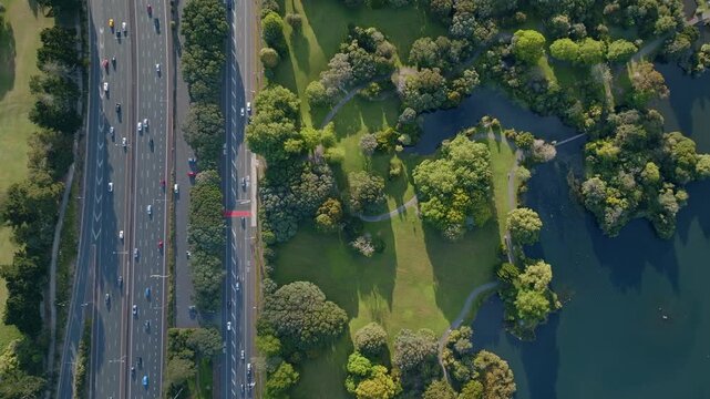 Aerial view of Western Springs, Auckland, New Zealand, showing a busy highway with cars and trucks, next to a green park with trees and a lake. Illustrates urban planning.