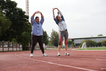 Two slim and plus size woman with sport jacket together stretch warm-up exercise on an outdoor running track, wellness and healthy lifestyle