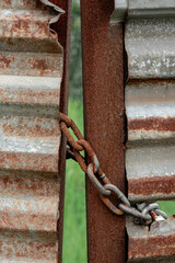 A rusty chain secures a weathered, corrugated metal gate to a corroded post.