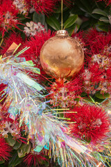 A gold coloured Christmas bauble and silver tinsel seen amongst the red flowers of a New Zealand Summer flowering  Pohutukawa tree. The tree is endemic to NZ and is known as the NZ Christmas tree. 