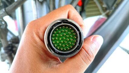 Close-up view of a multi-pin circular aviation connector held by a technician’s hand, showing...