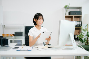 Confident Asian woman with a smile standing holding notepad and tablet at the modern office.