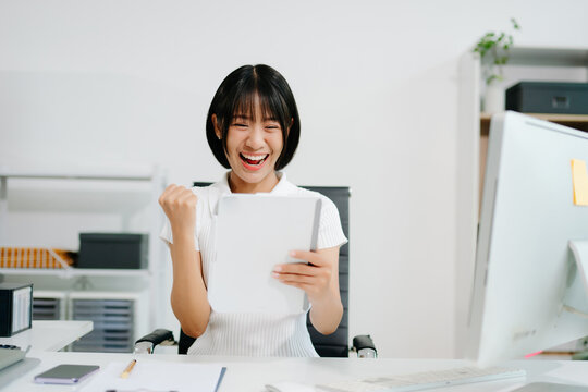 A cheerful office woman celebrating success at her desk, showing excitement, achievement, and positive workplace energy in office - Powered by Adobe