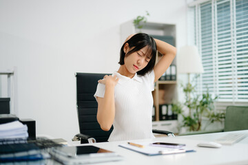 A young office woman suffering from neck and back pain while working at her desk, showing workplace...