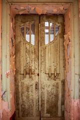 Grungy Art Nouveau entryway, a weathered double door with distinctive curved glass. Peeling paint and decay unveil the forgotten history of this historic manor