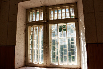Grungy multi-pane windows in a derelict structure, bathed in natural light. Peeling paint and dusty glass evoke a sense of abandonment and decay