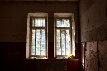 Sunlight streams through grungy barred windows in a derelict, dusty abandoned building, revealing a scene of forgotten decay