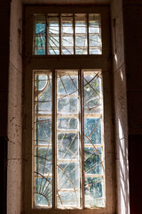 Sunlight pierces a grungy, broken window in a forgotten, crumbling manor. Fractured glass and dusty frames highlight urban decay and abandonment