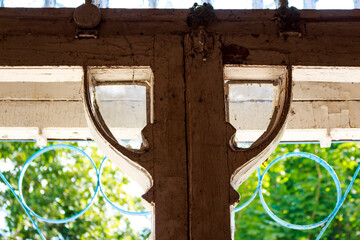 Ornate, crumbling Art Nouveau window frame from an abandoned mansion's interior, offering a glimpse of lush summer greenery through the antique glass