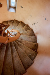 A grungy spiral staircase descends within a forgotten, abandoned early 20th-century manor. Dusty steps and peeling walls evoke a sense of bygone grandeur and decay
