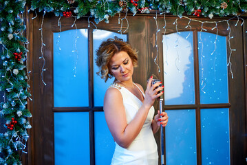 A woman in a white dress, standing in front of a Christmas tree, sings a song into a microphone, which is in her hands.