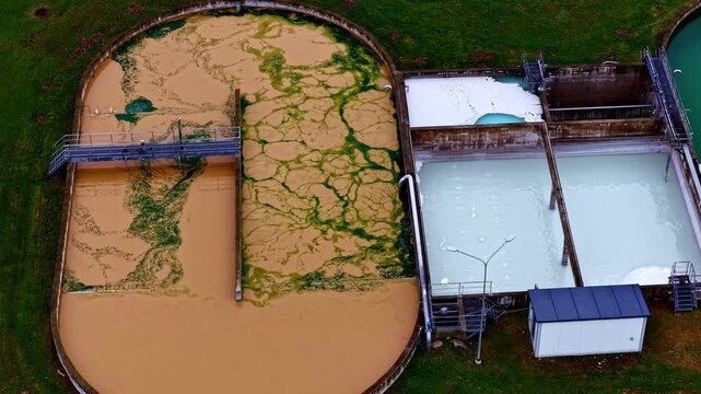 A circling aerial shot orbits industrial water treatment tanks, revealing algae patterns and sedimentation in a functional eco-facility.