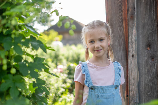 Young girl with pigtails smiles brightly in a lush garden, surrounded by greenery and sunlight, embodying the joy of summer and outdoor adventures with siblings
