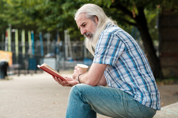 Senior man enjoying a book and coffee outdoors