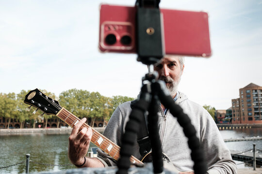 Musician streaming live guitar performance by the river - Powered by Adobe
