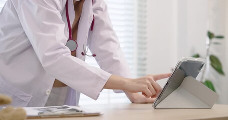 Closeup of Asian female doctor’s hands operating tablet on desk in clinic. Image captures modern digital healthcare process and focus on data handling in clinical work setting. - Powered by Adobe