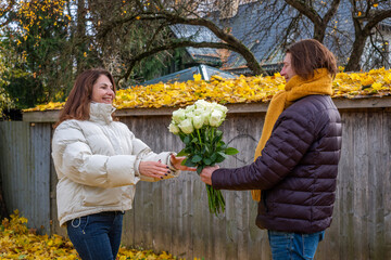 Midlife couple exchanging bouquet of white roses in autumn park, surrounded by vibrant yellow leaves, celebrating love and connection in a serene outdoor setting