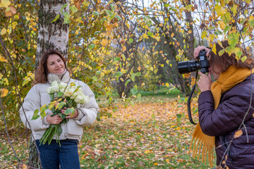 Midlife couple enjoying a romantic moment in autumn, surrounded by colorful leaves, as one partner captures the other holding roses, creating a warm and intimate atmosphere