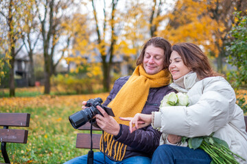 Midlife couple enjoying a romantic moment in autumn park, sharing laughter while looking at camera, surrounded by colorful leaves and holding roses, capturing love and joy